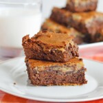 Two Caramel Cheesecake Brownies stacked on a white plate.
