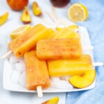 A white plate with Peach Lemonade Popsicles with slices of peach and lemon on the side.