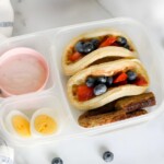 Lunch box of Waffle Tacos, hard boiled eggs, sausage, and yogurt.