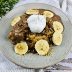 A plate of chocolate banana icebox cake garnished with six slices of bananas topped with whipped cream.