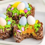 Chocolate Rice Krispies, one missing a bite, topped with sprinkles and chocolate egg sitting on a white plate.