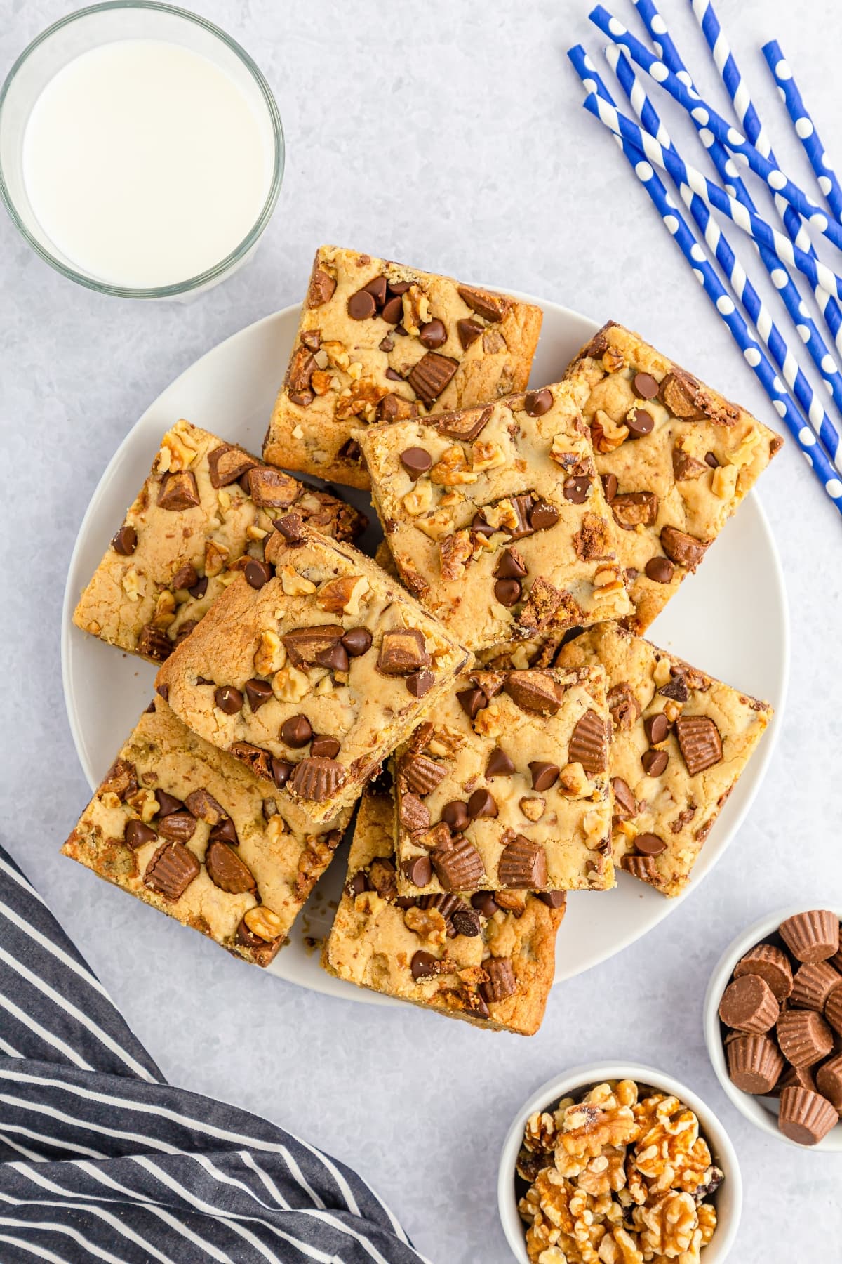 A stack of Cookie bars topped with chopped Reese’s peanut butter cups, chopped walnuts, and chocolate chips.