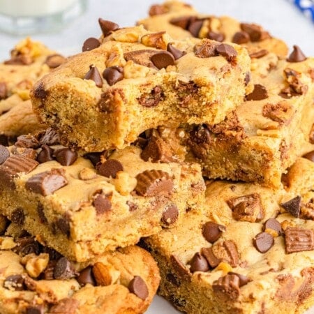 A pile of cookie bars topped with chopped Reese’s peanut butter cups, chopped walnuts, and chocolate chips.