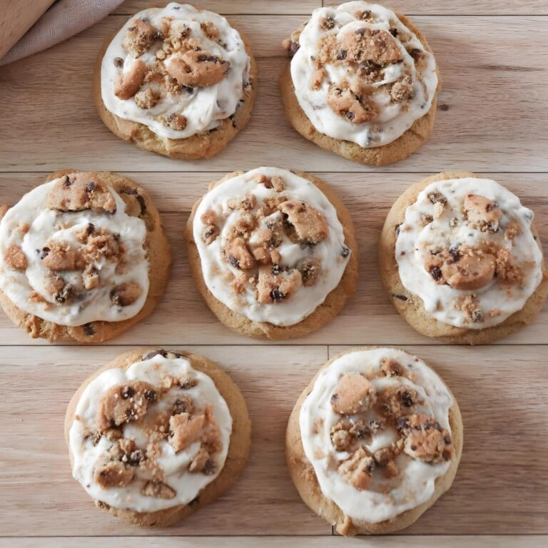 Chocolate chip cookie topped with frosting and Chips ahoy mini cookies on a wooden table.