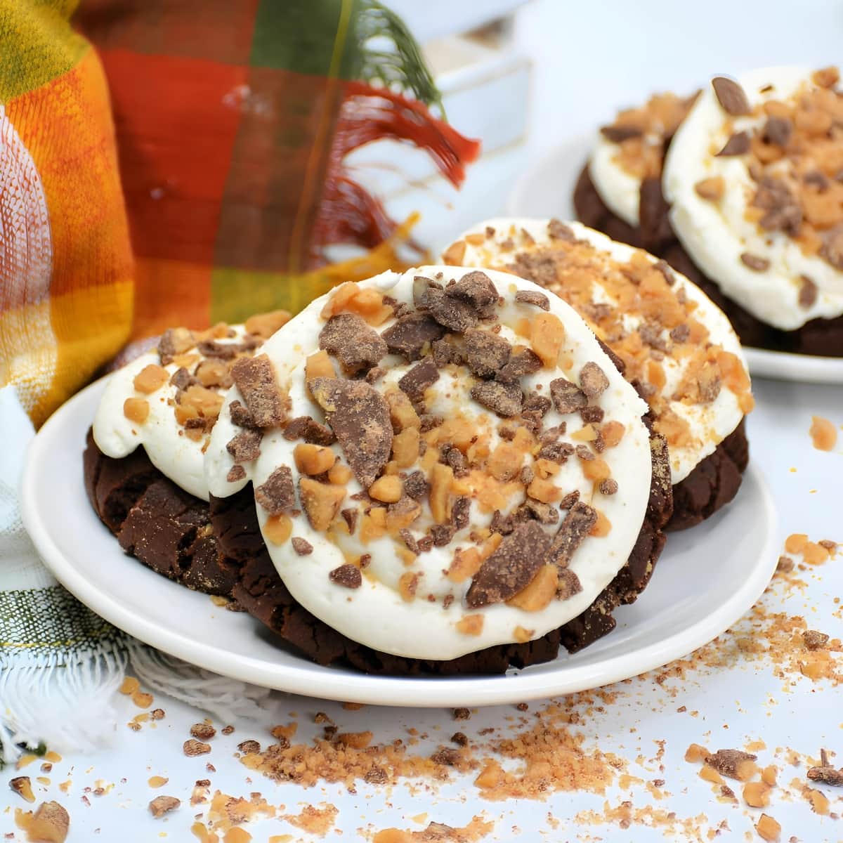 Chocolate cookies with vanilla frosting and chopped heath bars on top of a plate.