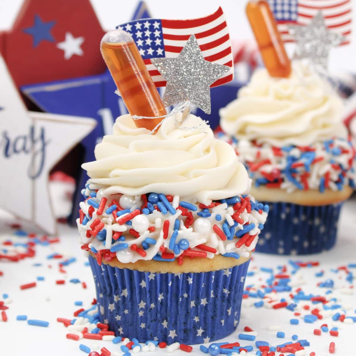 Patriotic themed cupcake with white, blue, and red sprinkles topped with mini pipette.