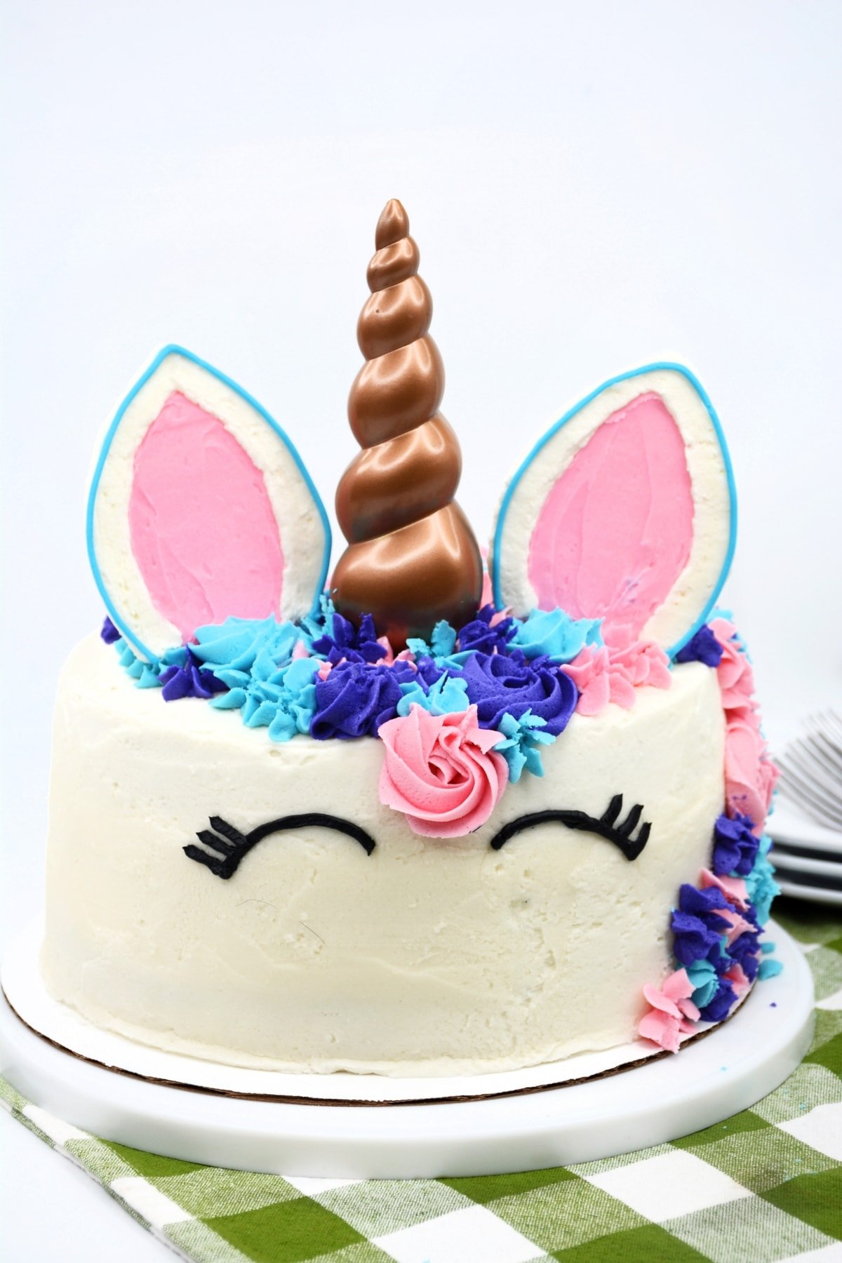Layered cake piped with purple, blue, and pink frosting added with plastic unicorn cake topper horn and ears.