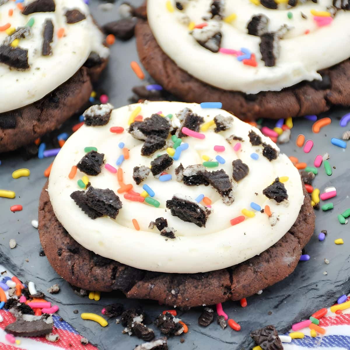Oreo cookies with white frosting topped with sprinkles and crushed oreas sitting on a board.