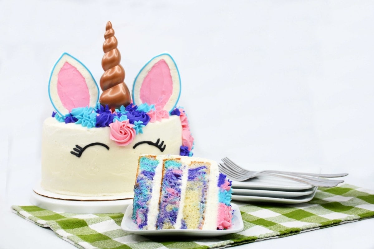 Layered cake with unicorn themed sitting on a table with green and white cloth.