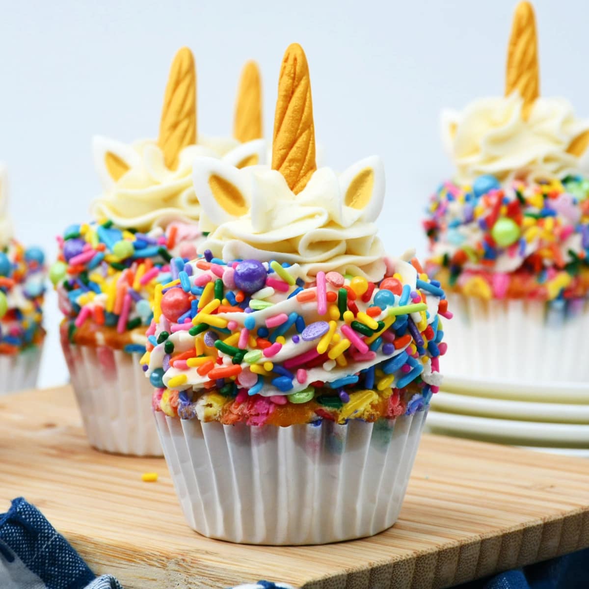 Cupcakes decorated to look like unicorns with white frosting, colorful sprinkles, and unicorn toppers.