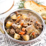 A bowl of ground beef stew with a piece of bread in the background.