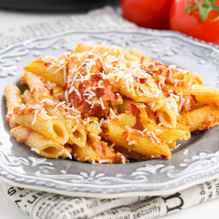 Penne pasta with vodka sauce topped with parmesan cheese and chili flakes on a silver plate.