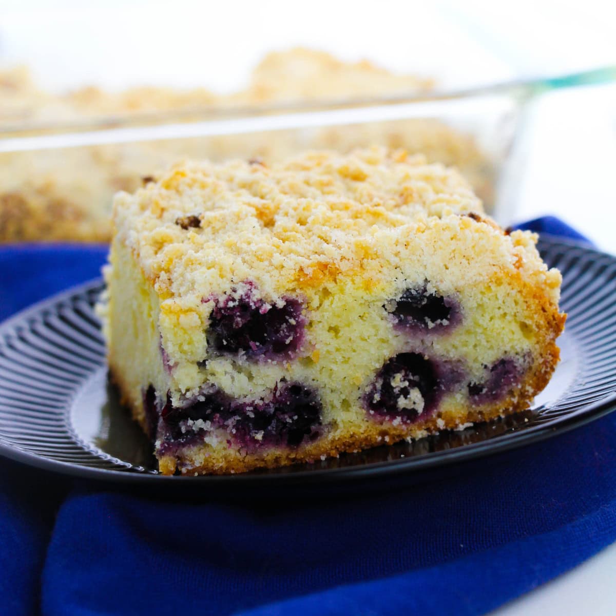 A black plate of Blueberry coffee cake sitting on a blue cloth.