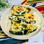 A white plate of Chicken enchiladas stuffed with poblano topped with melted cheese.