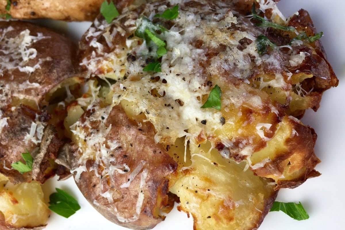 Crash Hot Potatoes sitting on a white plate topped with fresh parsley.