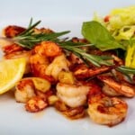 Lemon Garlic Jumbo shrimp topped with rosemary on a white plate.