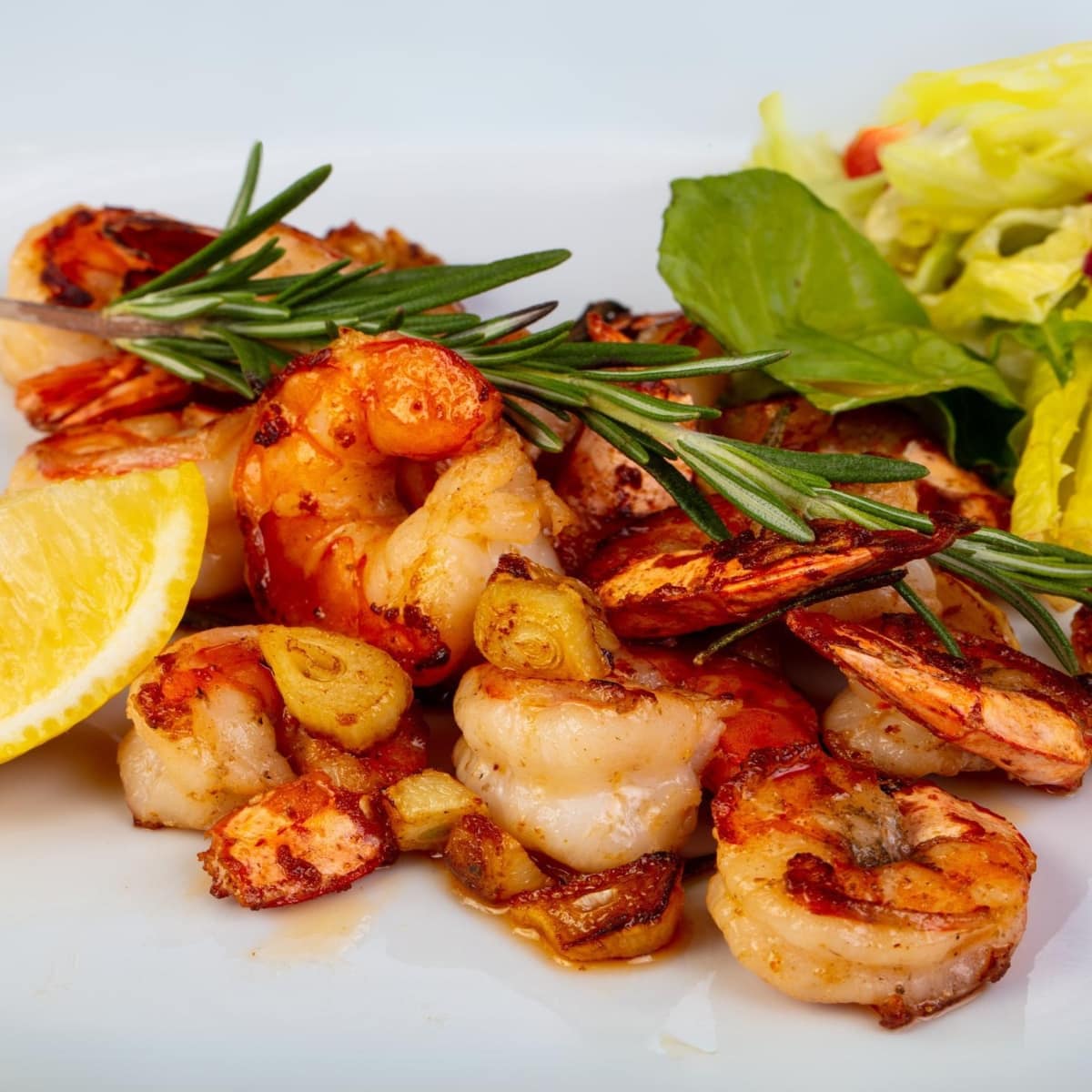 Lemon Garlic Jumbo shrimp topped with rosemary on a white plate.
