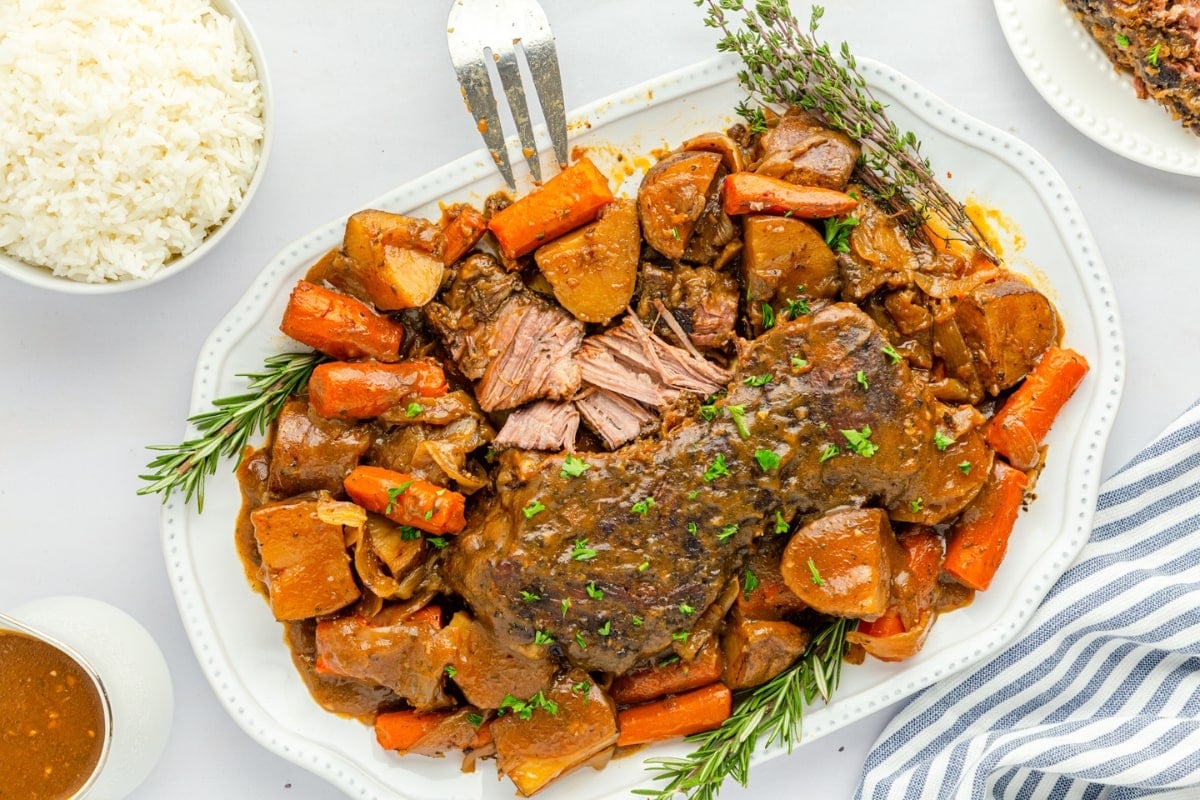 Pot Roast on a platter with carrots and potatoes on the sides garnished with thyme and parsley.