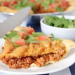 A slice of Taco Casserole on a white plate topped with chopped tomatoes and lettuce.