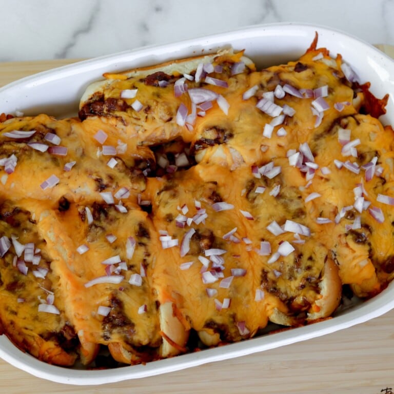 Chili Cheese Dog bake sprinkled with red onion in a white casserole dish.