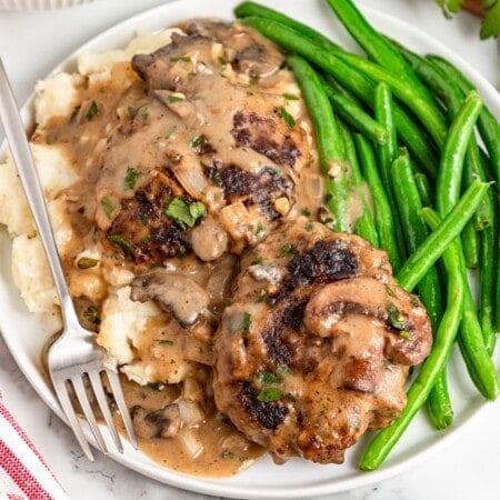 A white plate with Hamburger Steak and green beans on the sides.