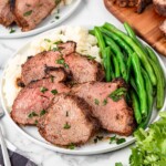 A plate of slices of tri tip with mashed potatoes and green beans.