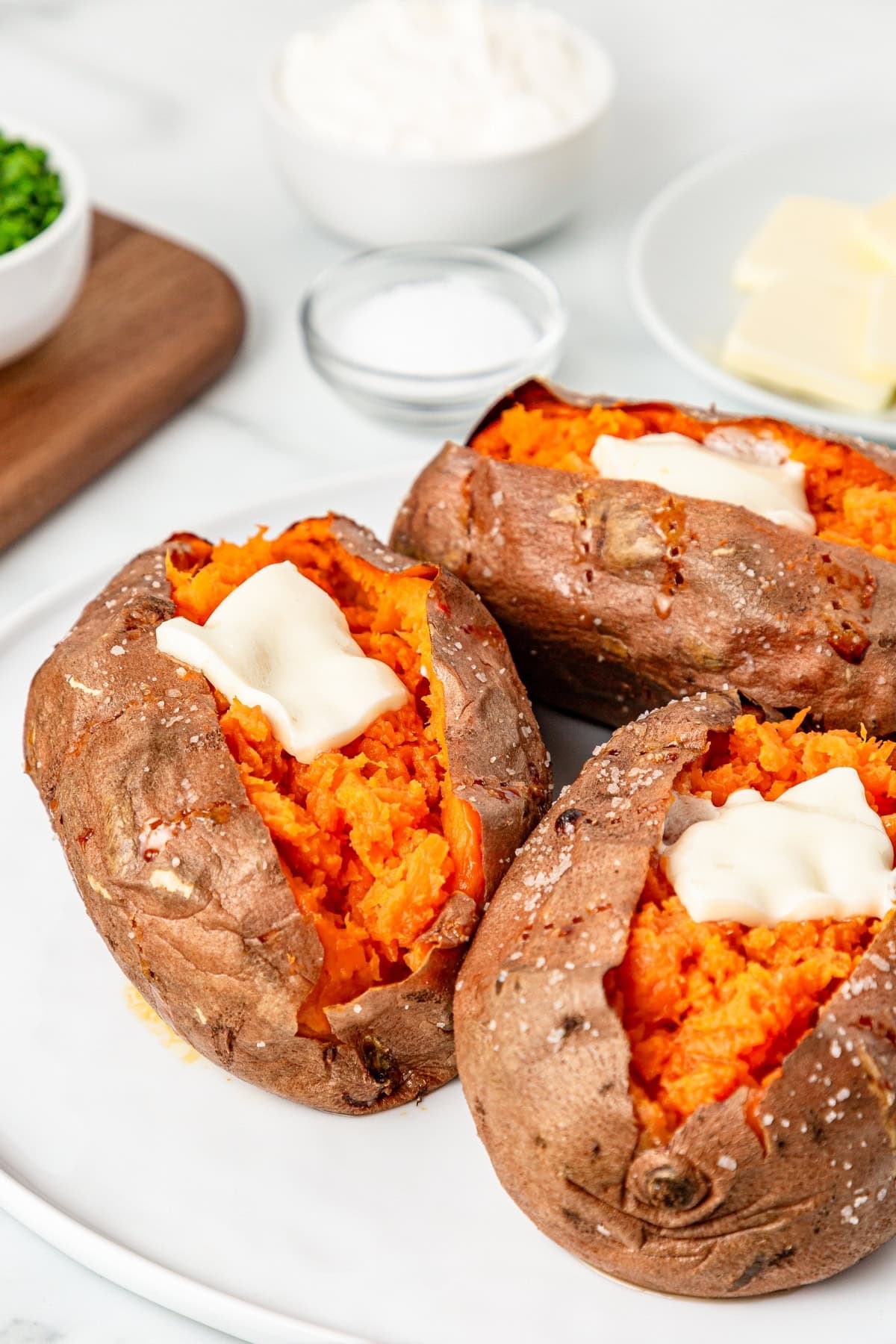 Three sweet potatoes with a slice of butter on top sitting on a white plate.