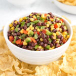 A bowl of black bean and corn salsa surrounded with chips.