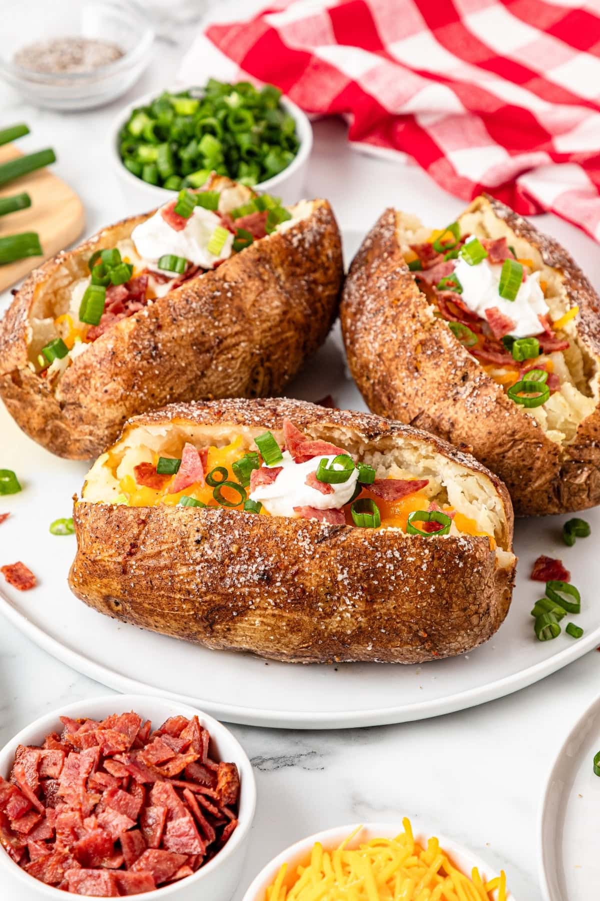 Three baked potatoes topped with shredded cheese, bacon, and sour cream.
