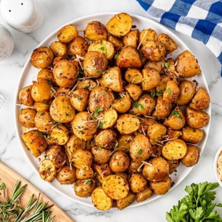 Roasted baby potatoes on a white plate topped with cheese and parsley.