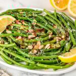 A plate of green beans with almonds and parmesan cheese with a slice of lemons on the side.