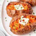 A plate of baked sweet potatoes with sour cream and chopped chives on top.