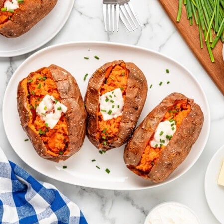 A white plate of three sweet potatoes with a slice of butter and a dollop of sour cream.