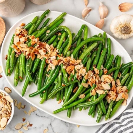 A white plate with green beans and almonds on top.