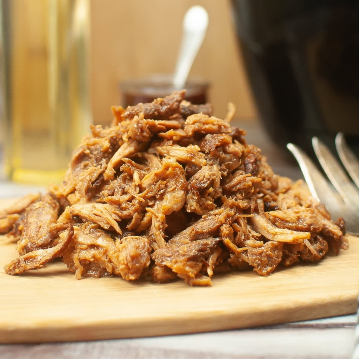 Pulled pork on a wooden board with a fork on the side.