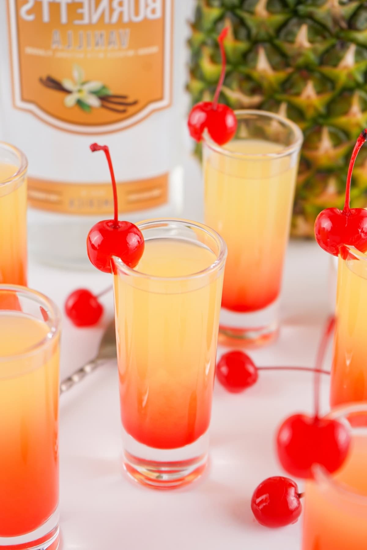Pineapple vodka in a shot glass garnished with maraschino cherry.