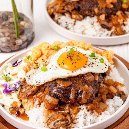 Hamburger patty with gravy topped with egg on a bed of rice with coleslaw and mac and cheese on the sides.