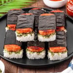 A rice with rice seasoning and spam wrapped into roasted seaweed sitting on a black plate.