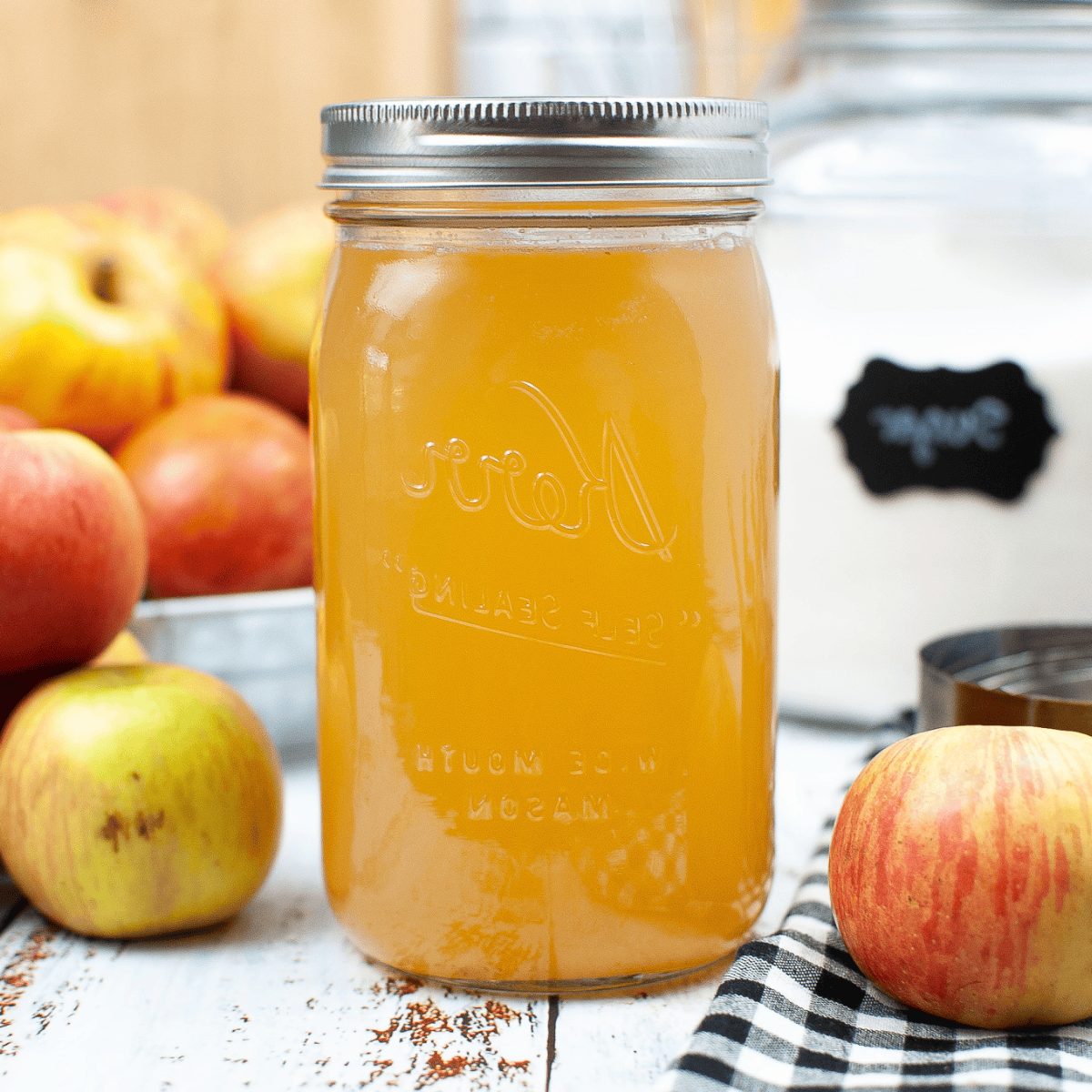 A glass jar of apple cider vinegar with fresh apples on the sides.