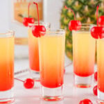 Pineapple vodka with grenadine in a shot glass with maraschino cherry on the rim.