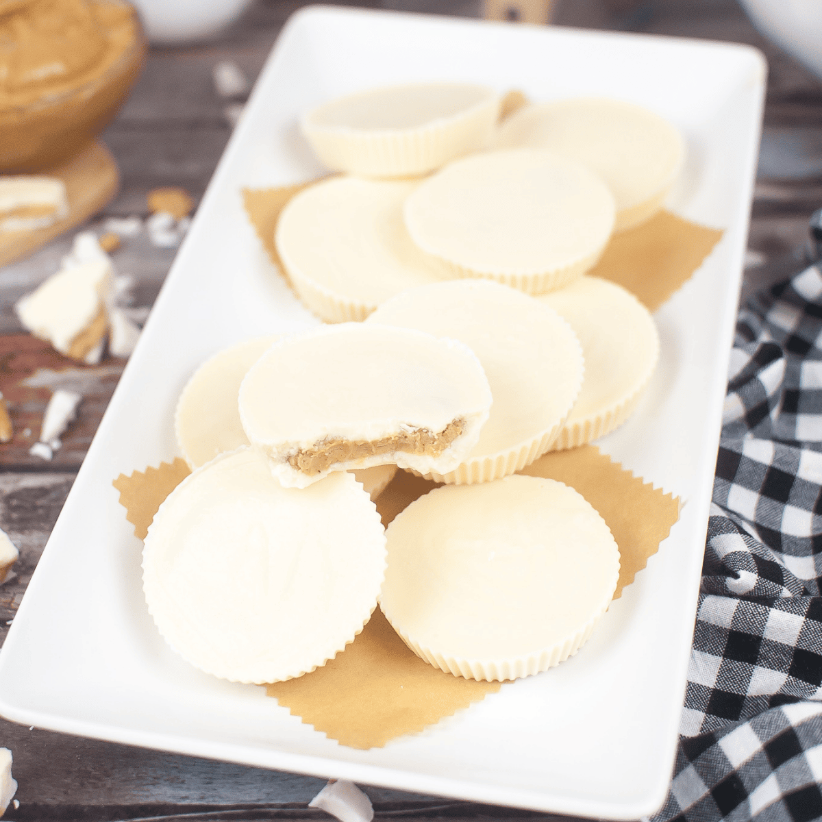 A plate of white chocolate peanut butter cups with a bite on it sitting on a wooden table.