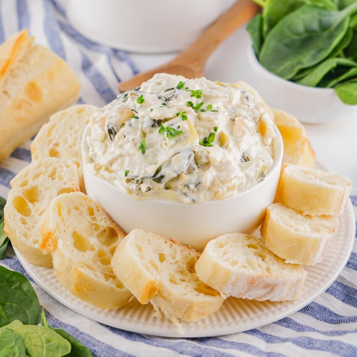 A white bowl of spinach artichoke dip with slices of French bread.