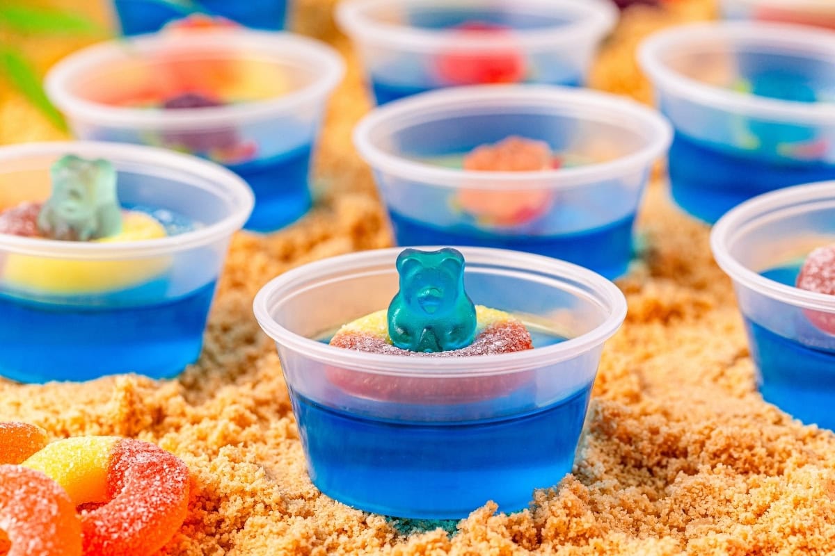 A small cup of blue gelatin topped with a gummy bear placed in the middle of a peach ring.