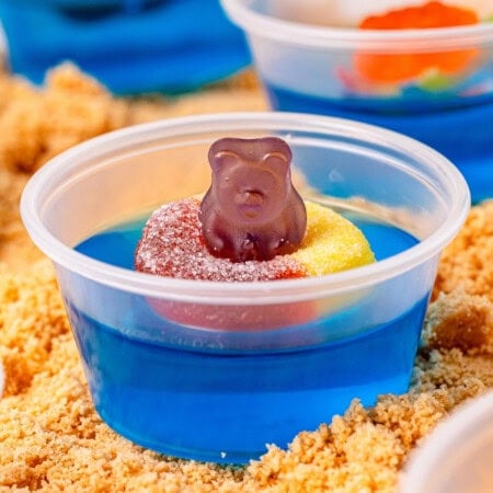 Blue jello shot in a small plastic container topped with a gummy ring and gummy bear.