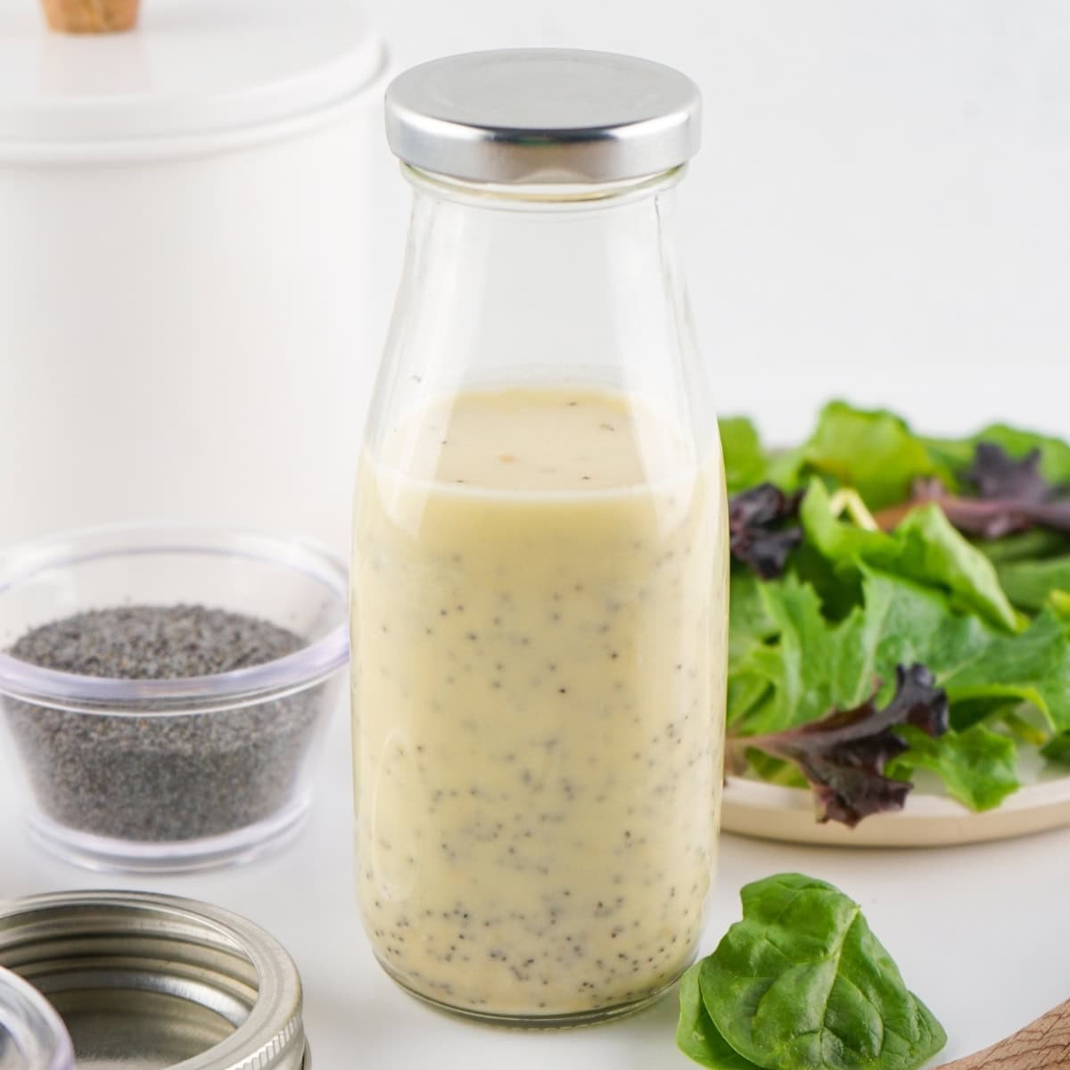 A glass bottle of Poppy Seed Dressing with a salad in the background.