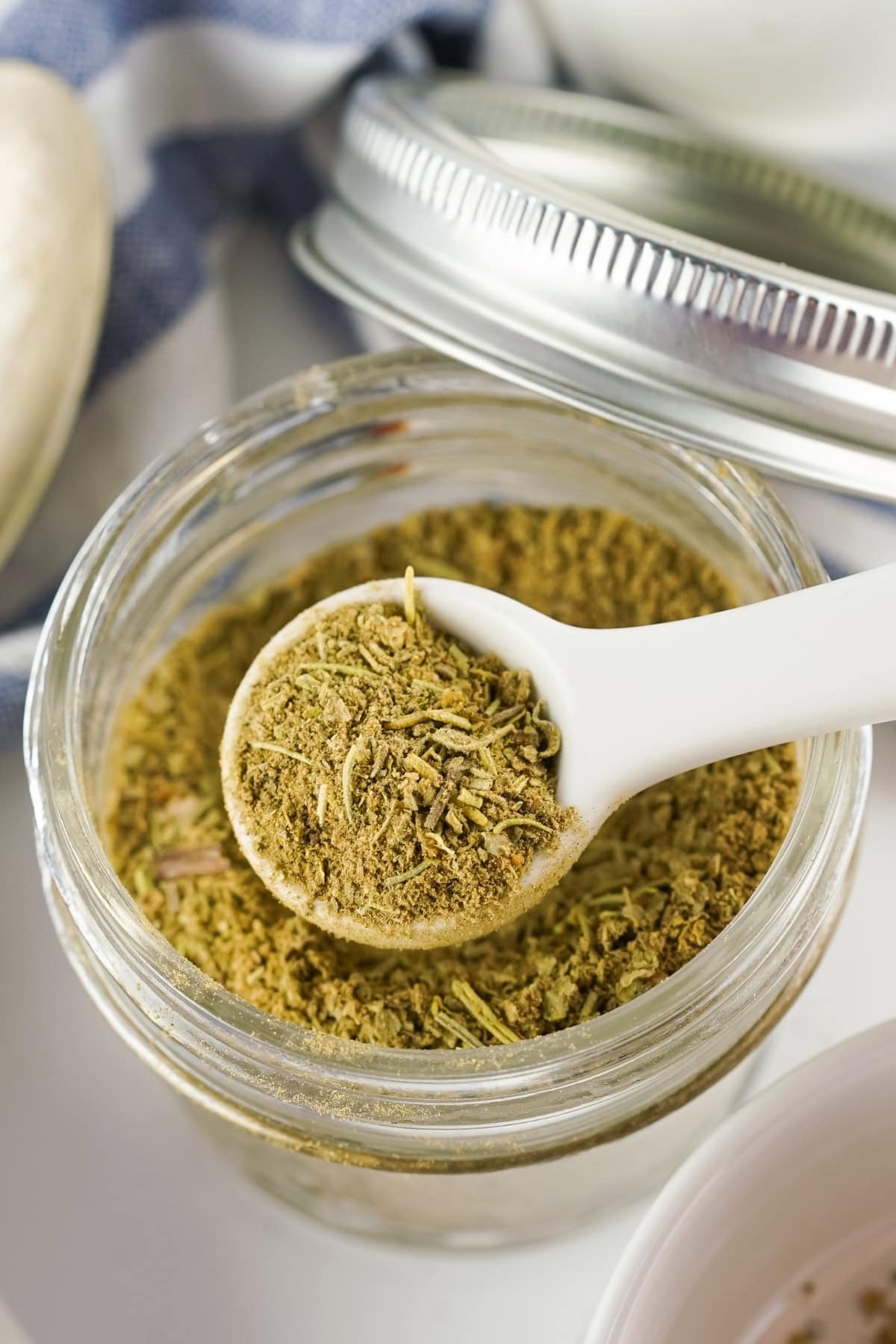 A measuring spoon scooping a poultry seasoning in an air tight container.