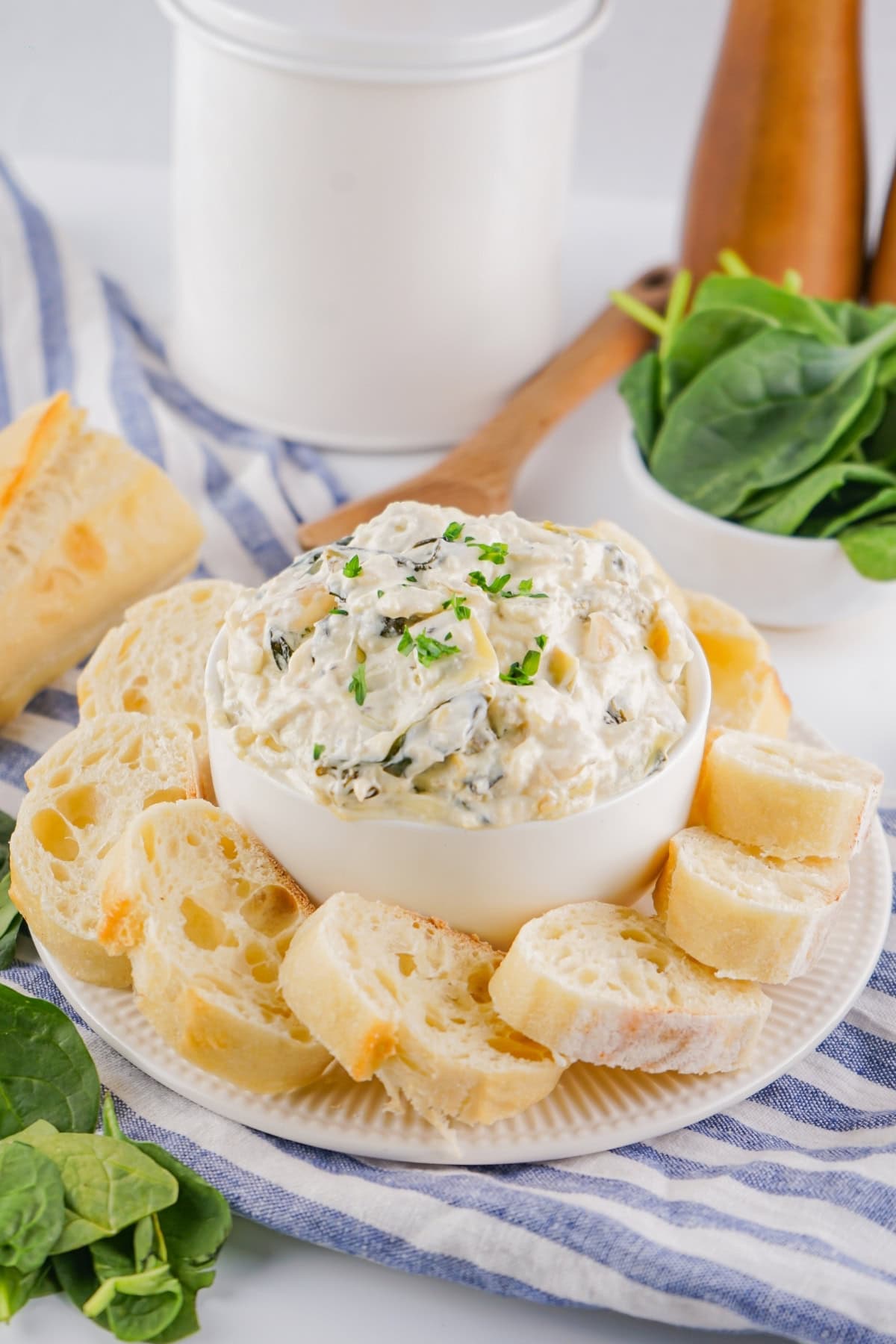 Spinach artichoke dip in a white bowl served with French bread slices on the sides.