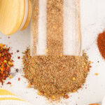 An air tight container with jerk seasoning mix spilled on a countertop.