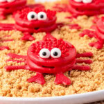 Crab themed Oreo cookies sitting on a white plate with crushed Oreos to look like sand.