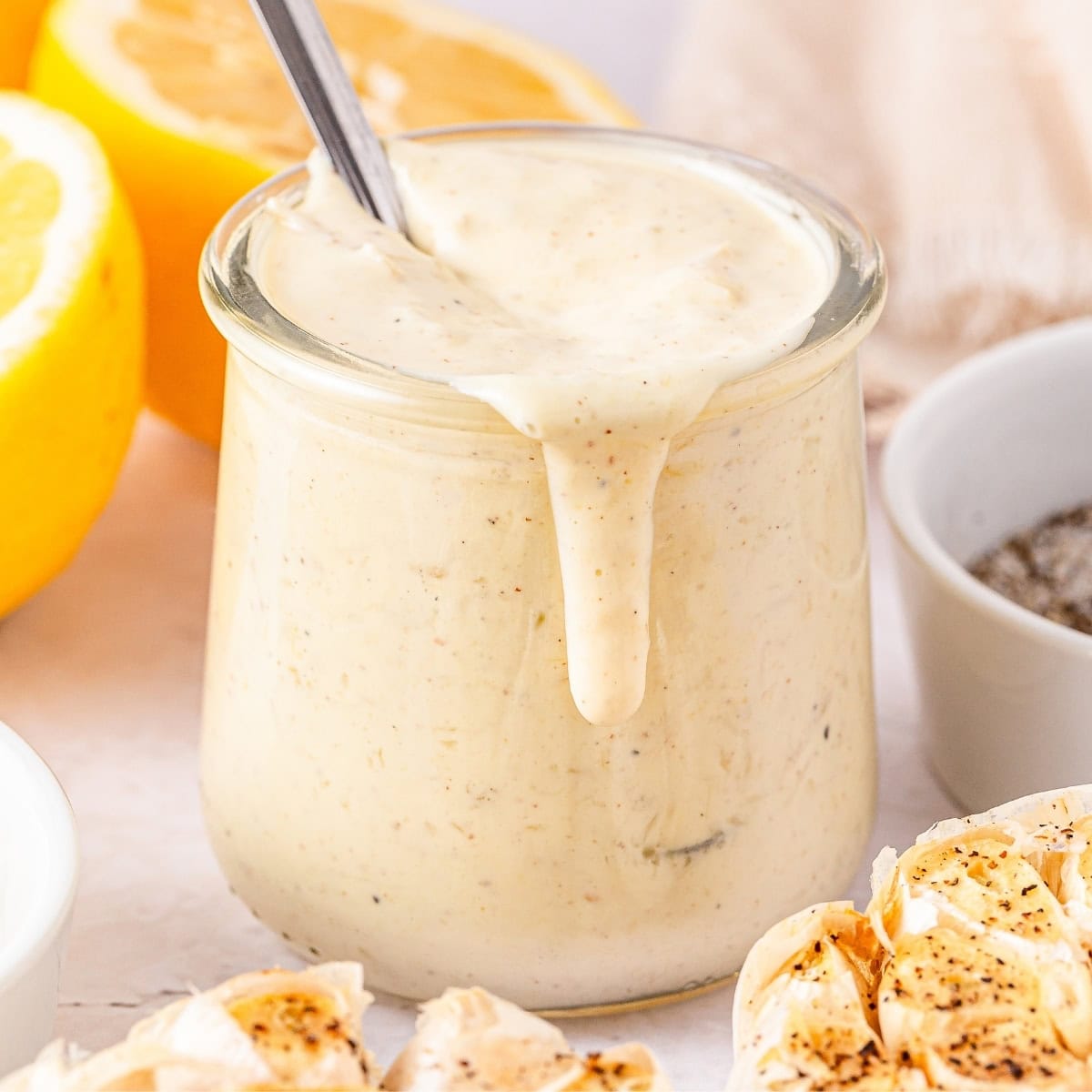 A glass jar of garlic aioli with a spoon inside.